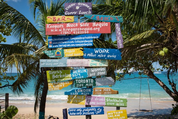 Humorous directional beach signs along side a beautiful sandy beach in Bequia Caribbean.